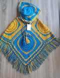 Poncho de crochê com capuz Kukini co. em azul e amarelo, destacando o tecido colorido e detalhes do design.