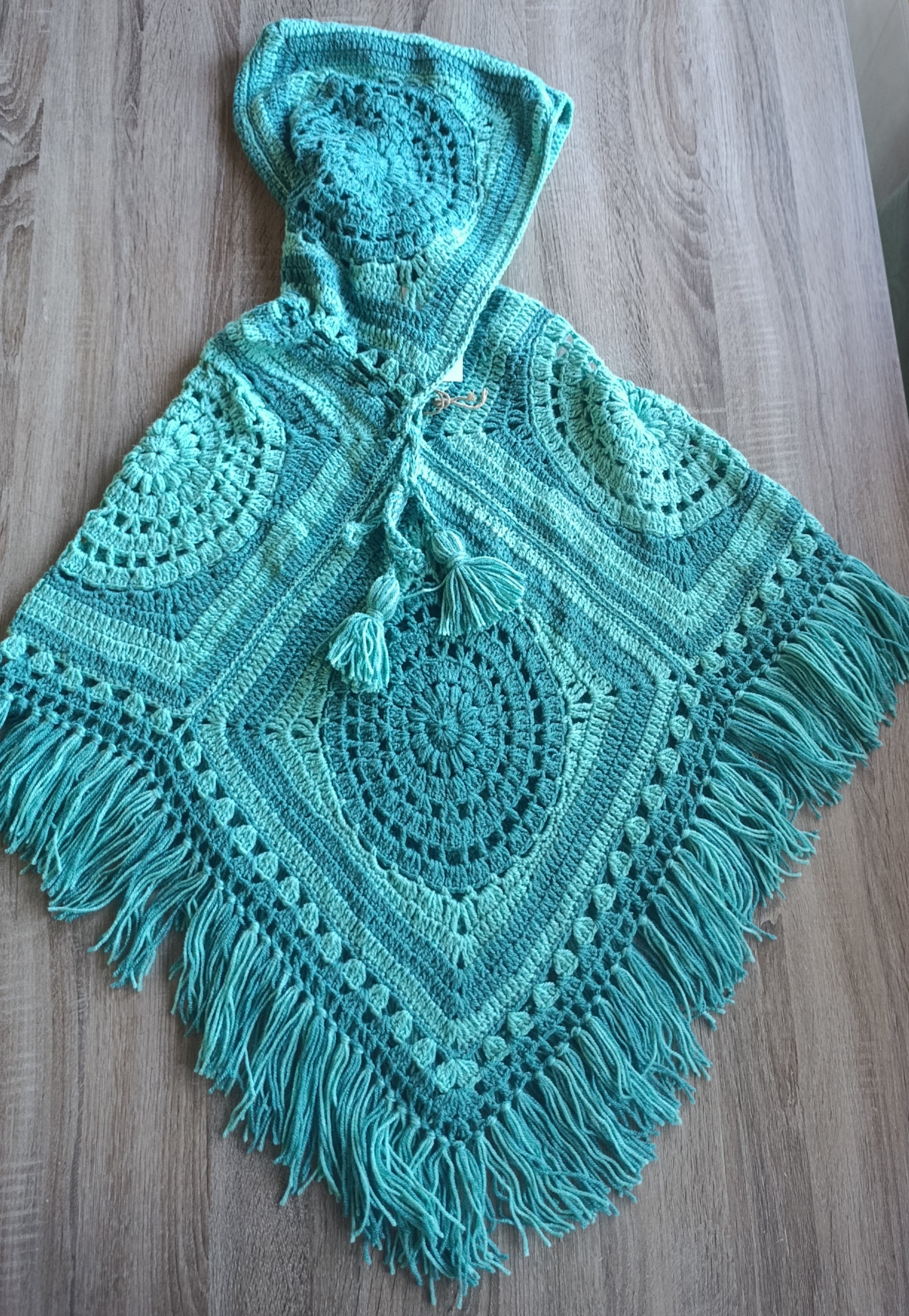 Poncho de crochê com capuz na cor hortelã, da marca Kukini Co., tecido confortável e estilo casual para dias frios.