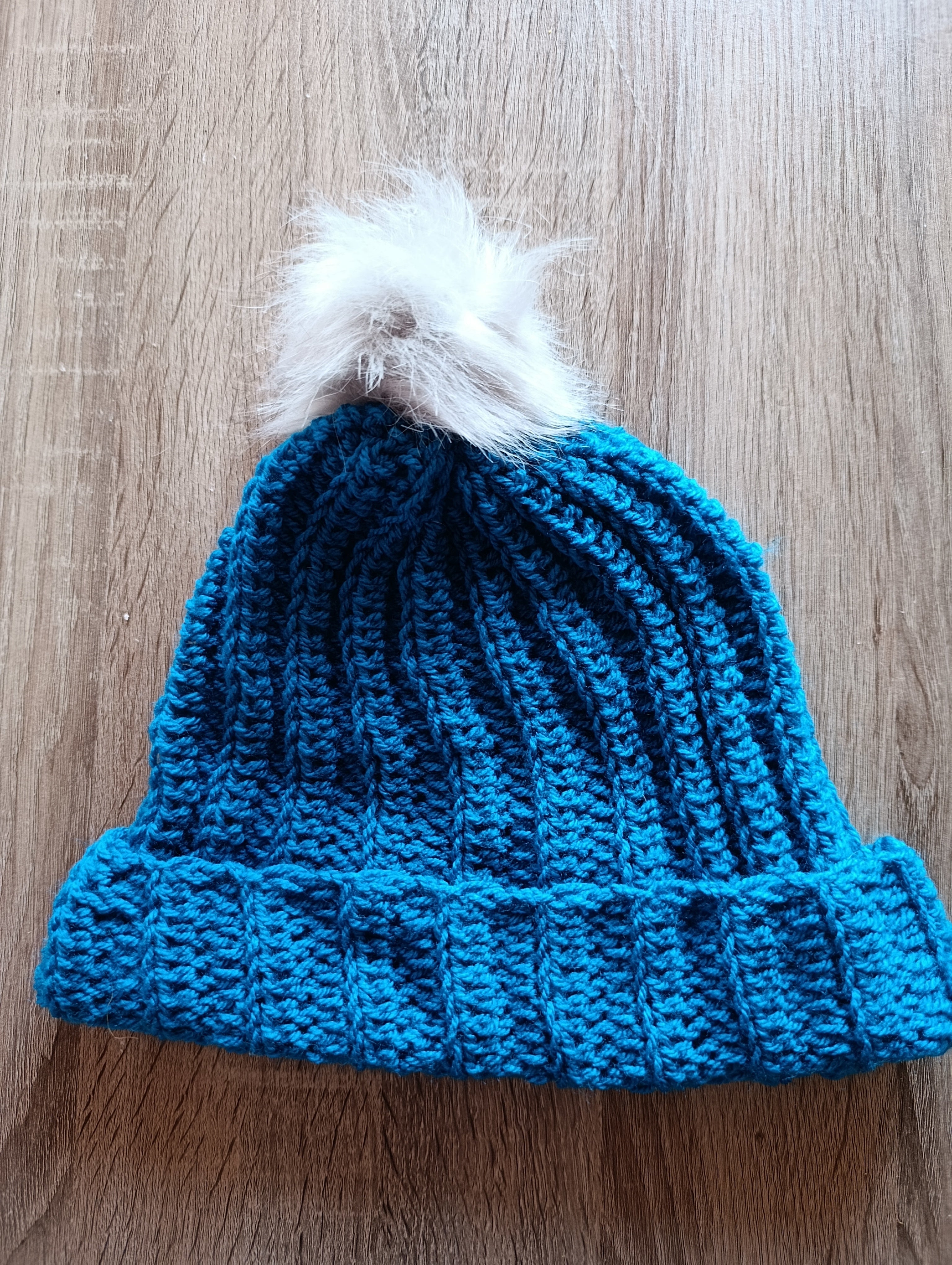 Gorro de crochê azul petróleo com pompom da Kukini Co., detalhe de acabamento e textura do material.