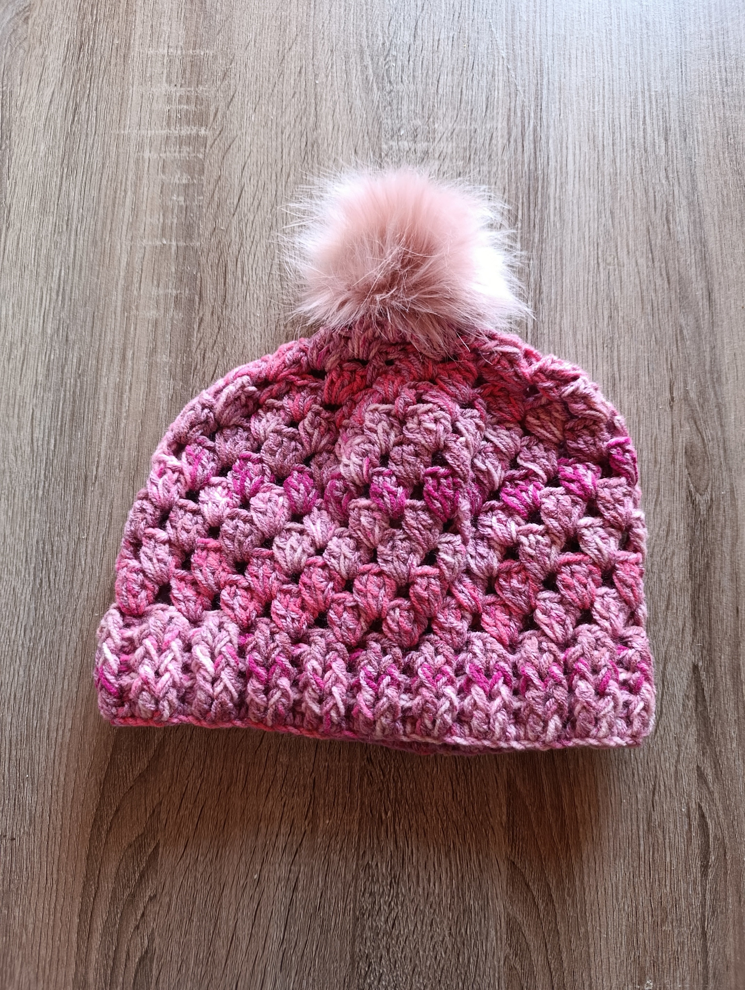Gorro de crochê granny square rosa com pompom da Kukini Co., mostrando detalhes do padrão colorido e acabamento macio.