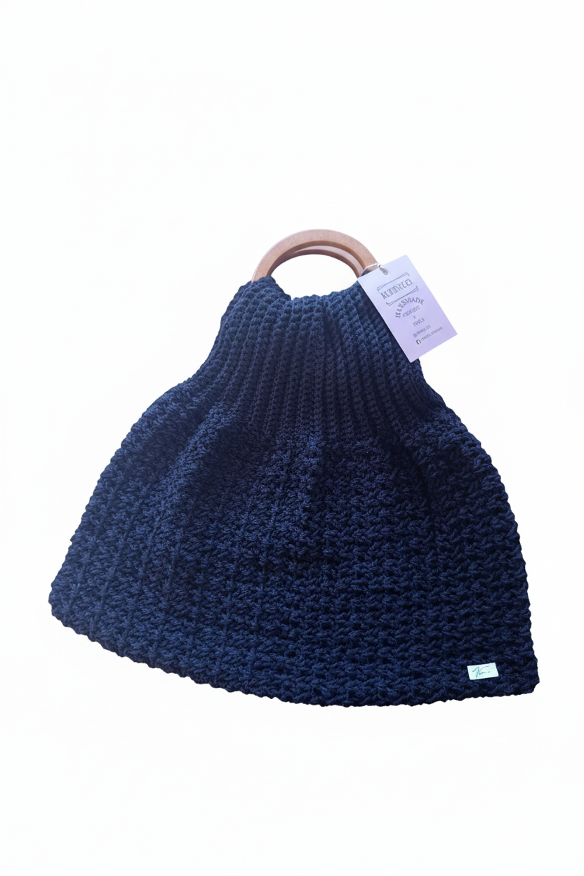 Bolsa de crochê preta com detalhe de arco, feita pela Kukini Co., exibida em fundo neutro.