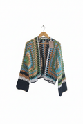 Cardigan de crochê Granny Square verde, azul e preto da Kukini Co., detalhes de pontos e cores vibrantes visíveis na imagem.